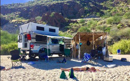 a lady sunbathing next to a pop up truck camper in the mountains