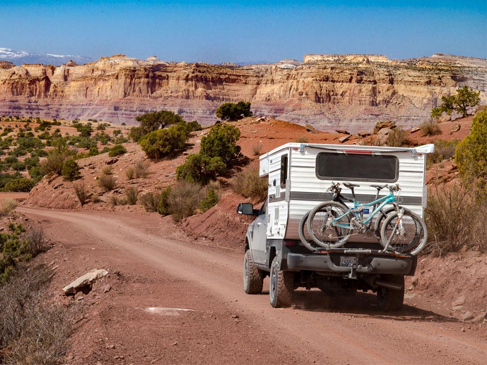 truck with pop up camper and bicycles mounted to the back driving through the desert