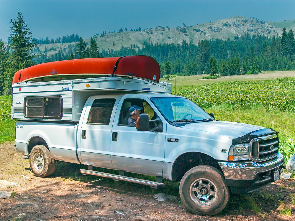 campers sitting in a truck with a pop up camper and canoe tied to roof