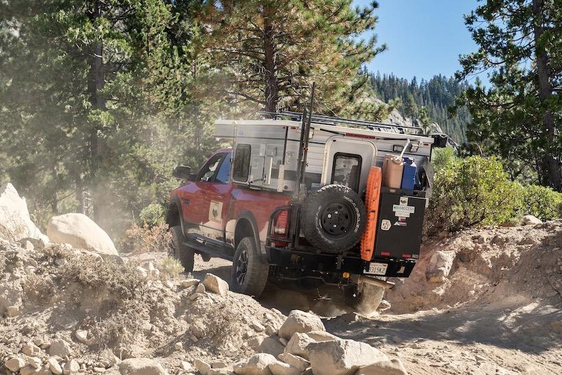 red dodge ram truck with slide-in pop camper in the bed driving over rocks